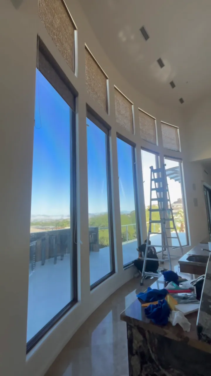 Crew tinting a curved wall of tall windows, ladder and tools at the base